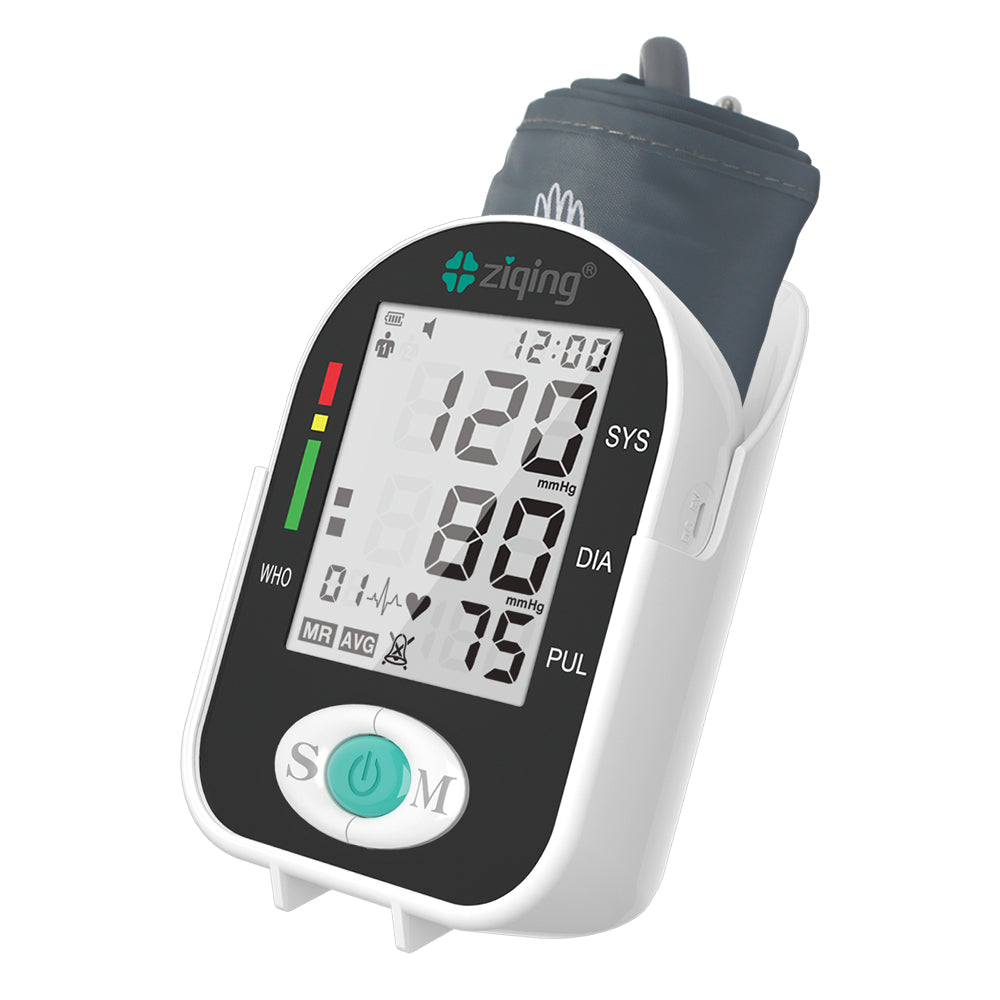 A digital blood pressure monitor with an LCD screen displaying readings, mounted on a white wall or surface, with a dark cuff attached to it.